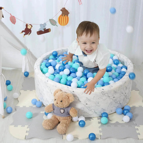 Child playing in a marble-patterned ball pit filled with blue and white plastic play balls, surrounded by toys, featuring Ball Pit Balls for Kids.