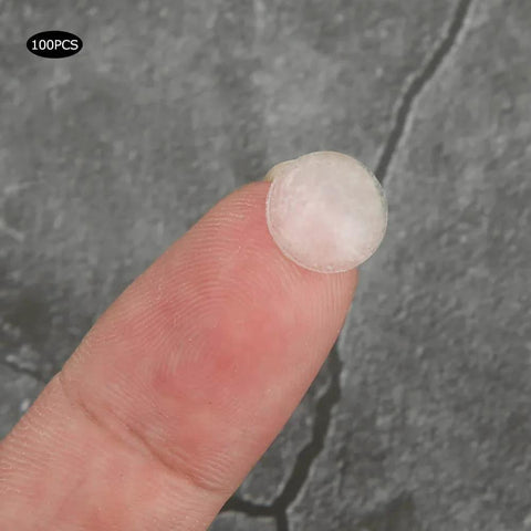 Close-up of a single transparent silicone bumper on fingertip, from Self Adhesive Anti Slip Silicone Bumpers 200 Pcs Transparent Foot Pads For Furniture Glass Displays Appliances And Hardware Anti Skid Shock Absorption Easy Peel And Stick Clear Cushions To Protect Surfaces Reduce Noise And Vibration.