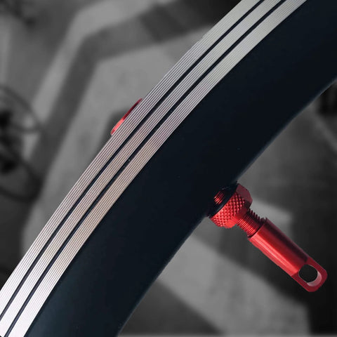 Red aluminum tubeless Presta valve stem installed in bicycle rim with knurled adjustment nut.