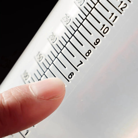Close-up of Two Stroke Oil Measuring Cup 16 Oz Mixing Pitcher With 15 In 1 Ratio Conversion Chart showing measurement marks and finger pointing
