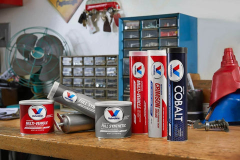 Various tubes and cans of Valvoline lubricants, including Valvoline - VV986 Moly-Fortified Gray Full Synthetic Grease 1 LB, on a workbench.