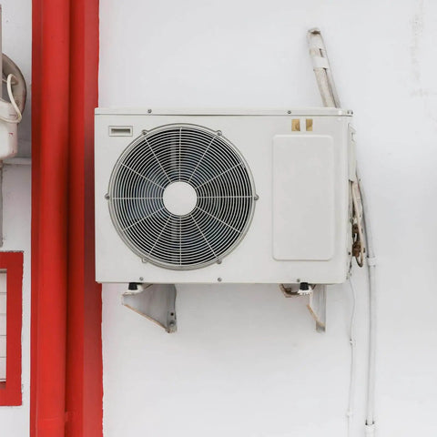 External air conditioning unit mounted on a wall with white and red surroundings