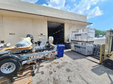 Outdoor view of a warehouse with a partially assembled trailer and Yamaha crates, surrounded by various equipment and vehicles.