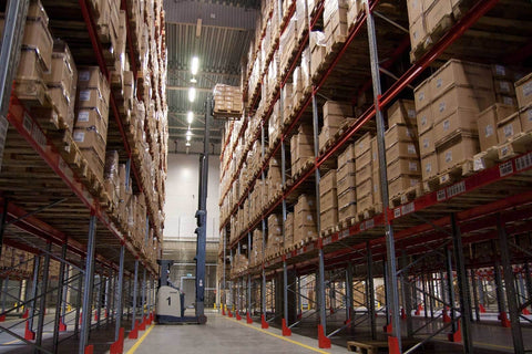 Warehouse storage with high racks filled with stacked boxes and a forklift in the aisle.