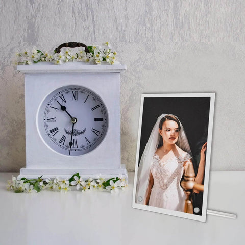 Decorative white clock with flowers beside framed bridal portrait on stand