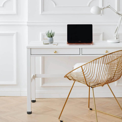 Modern office setup with white desk, laptop, gold wire chair, and adjustable furniture levelers for stable, balanced setups.