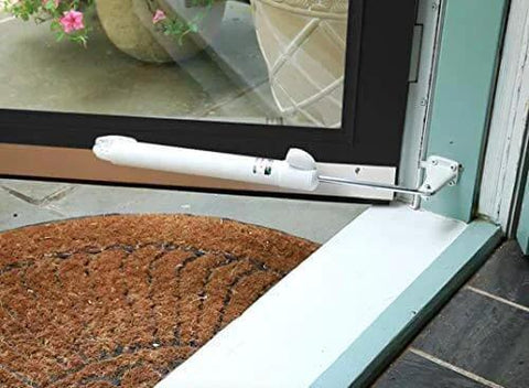 Heavy Duty Door Closer System (White) installed on a glass door with a patio view and brown doormat in the foreground.