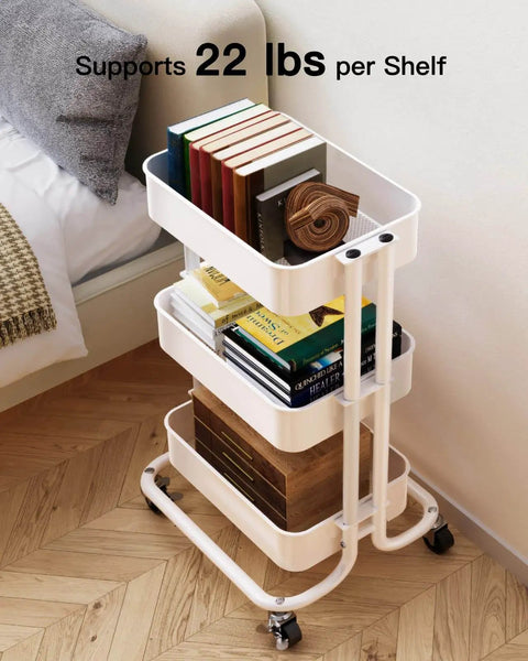 Three Tier Metal Rolling Utility Cart by Pipishell A Workhorse On Wheels With Two Lockable Wheels Great For Kitchen Dining Room And Living Room Storage And Organization Heavy Duty Mesh Shelves Mobile Serving Cart In White with books on tiers next to a couch.