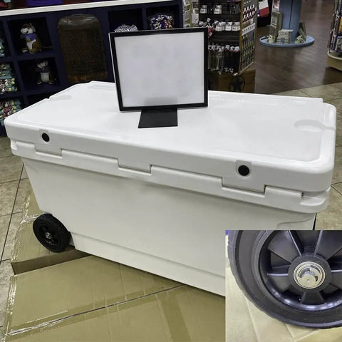 Large white rolling cooler with closed lid and visible wheel on store floor, displayed with a blank sign.