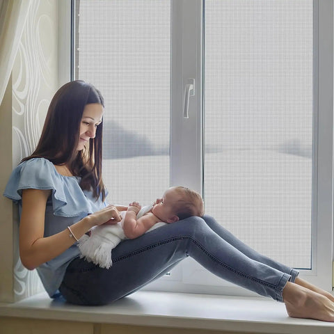 Woman sitting by window with baby, showcasing 48 X 102 Inch Fiberglass Window Screen Mesh for Windows and Doors Replacement Screen Door Mesh in Black Durable UV Protected Outdoor Screen.