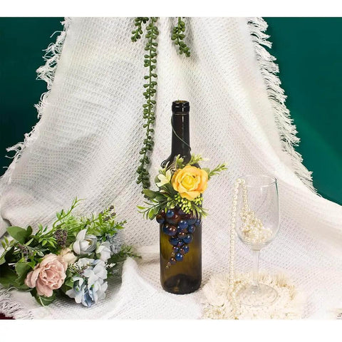 Decorative wine bottle with yellow rose and berries against white fabric backdrop with greenery and flowers