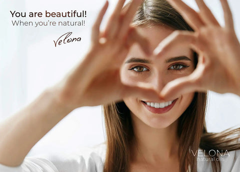 Smiling person forming heart shape with hands in bright background, text reading 'You are beautiful' and 'Velona natural oils'