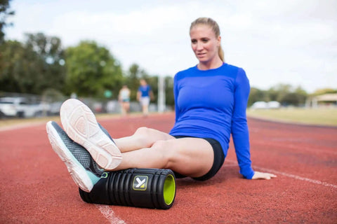 Woman using Grid 1.0 Multi Density Foam Roller for deep tissue massage on athletics track, 13 inch roller for muscle recovery and mobility