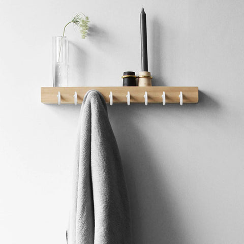 Wall-mounted shelf with hooks holding a candle, vase with flower, and gray towel