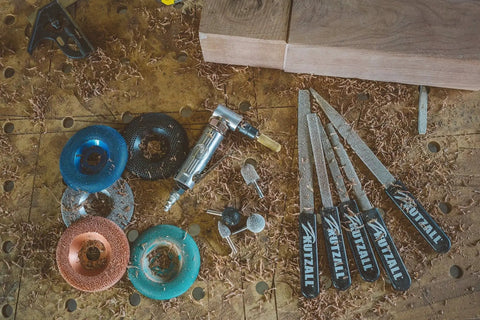 Assorted woodworking tools including an angle grinder attachment, files, and abrasive discs on a workbench.