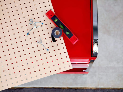 Pegboard with hooks and level placed next to Extreme Double Sided Mounting Tape 414H, near a red tool cart.