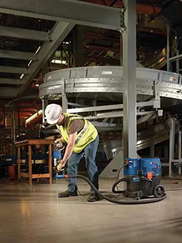 Worker using One And One Eighth Inch SDS-Plus Bulldog Xtreme Max Rotary Hammer for concrete drilling in a factory setting.