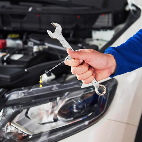 A hand holding a wrench near a car engine, using Three Pack 18G Grease Gun Needles For Easy Lubrication Of Machines And Bicycle Chains.