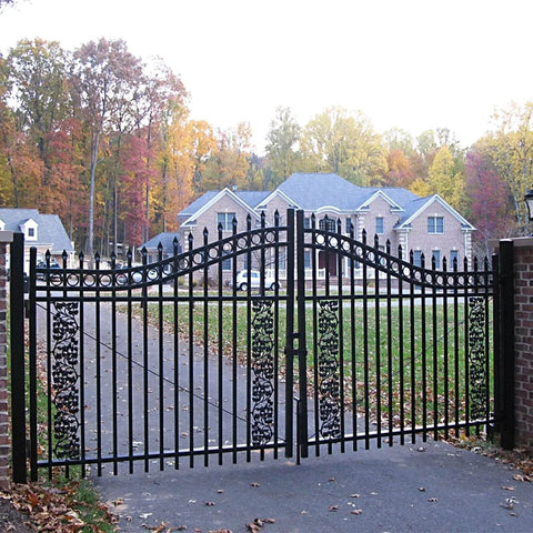 Elegant black wrought iron driveway gate with autumn trees, showcasing an upscale home in the background.