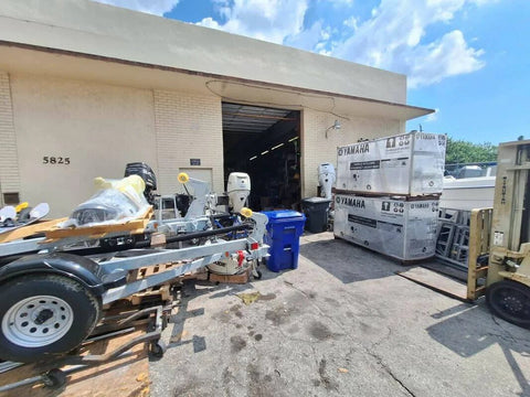 Warehouse exterior with marine equipment and boxed Yamaha motors outside, near open garage door.