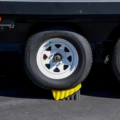 Trailer wheel supported by Curved Camper Leveler and Wheel Chock for RVs and trailers up to 30,000 lbs by Camco.