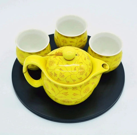 Yellow teapot and cups on black turntable platform.